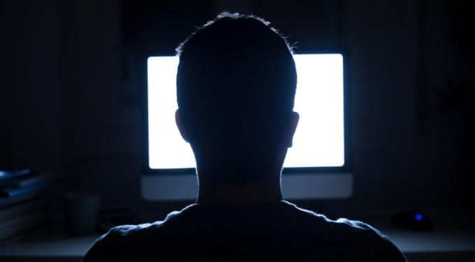 Mann von hinten vor Computer Bildschirm im dunklen Raum
