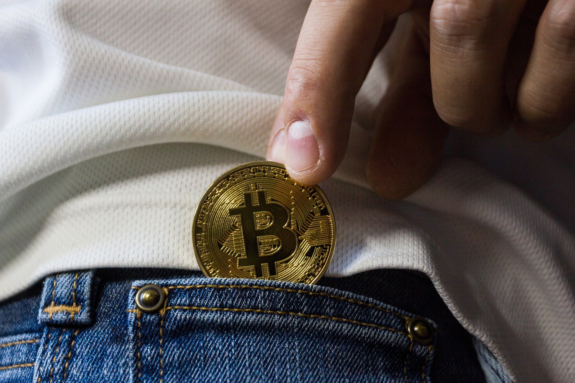 Eine Bitcoin Münze, die aus der Hosentasche gezogen wird.