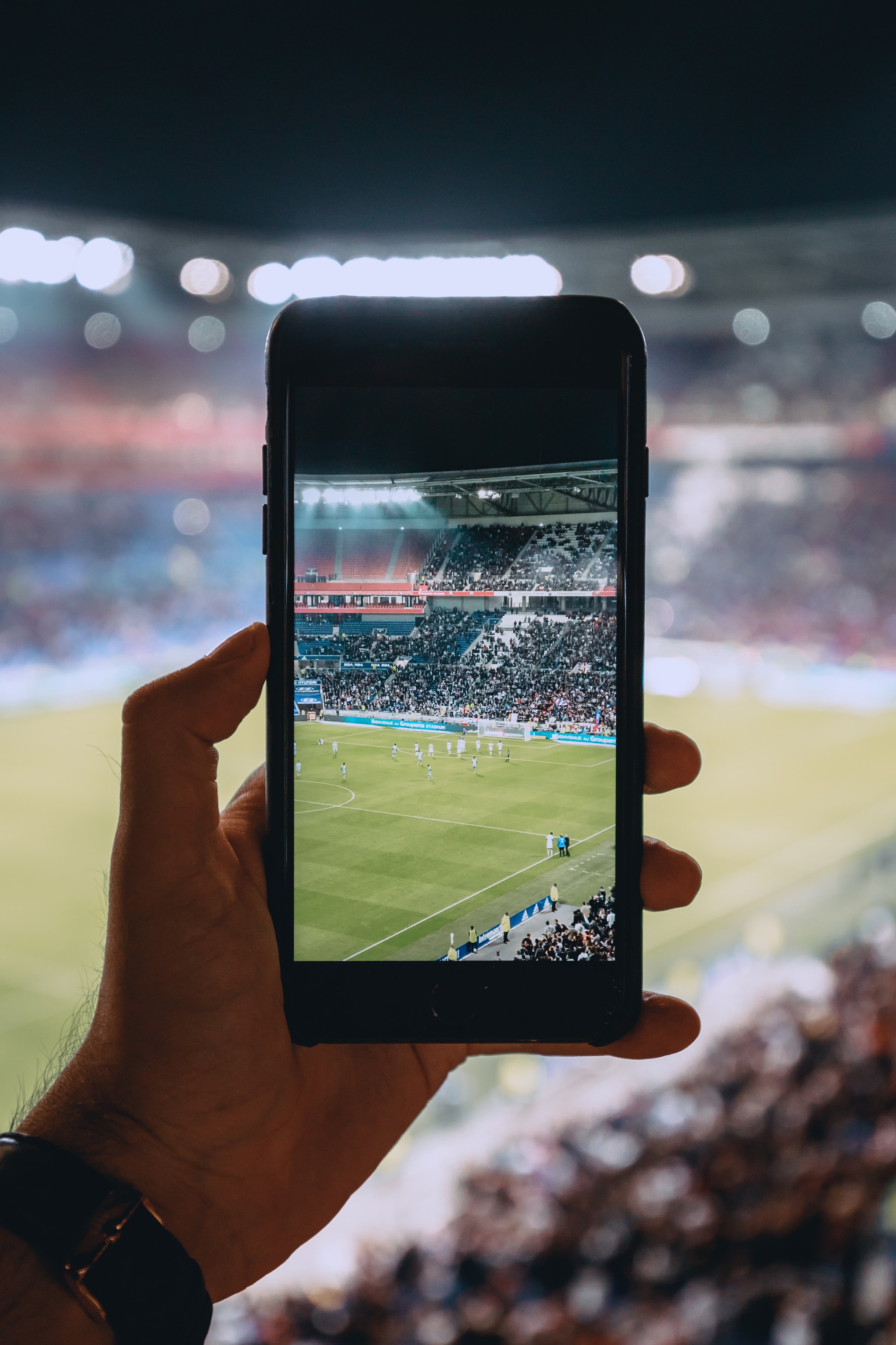 Blick auf den Rasen eines Fußballstadions durch Kamera und Display eines Smartphones