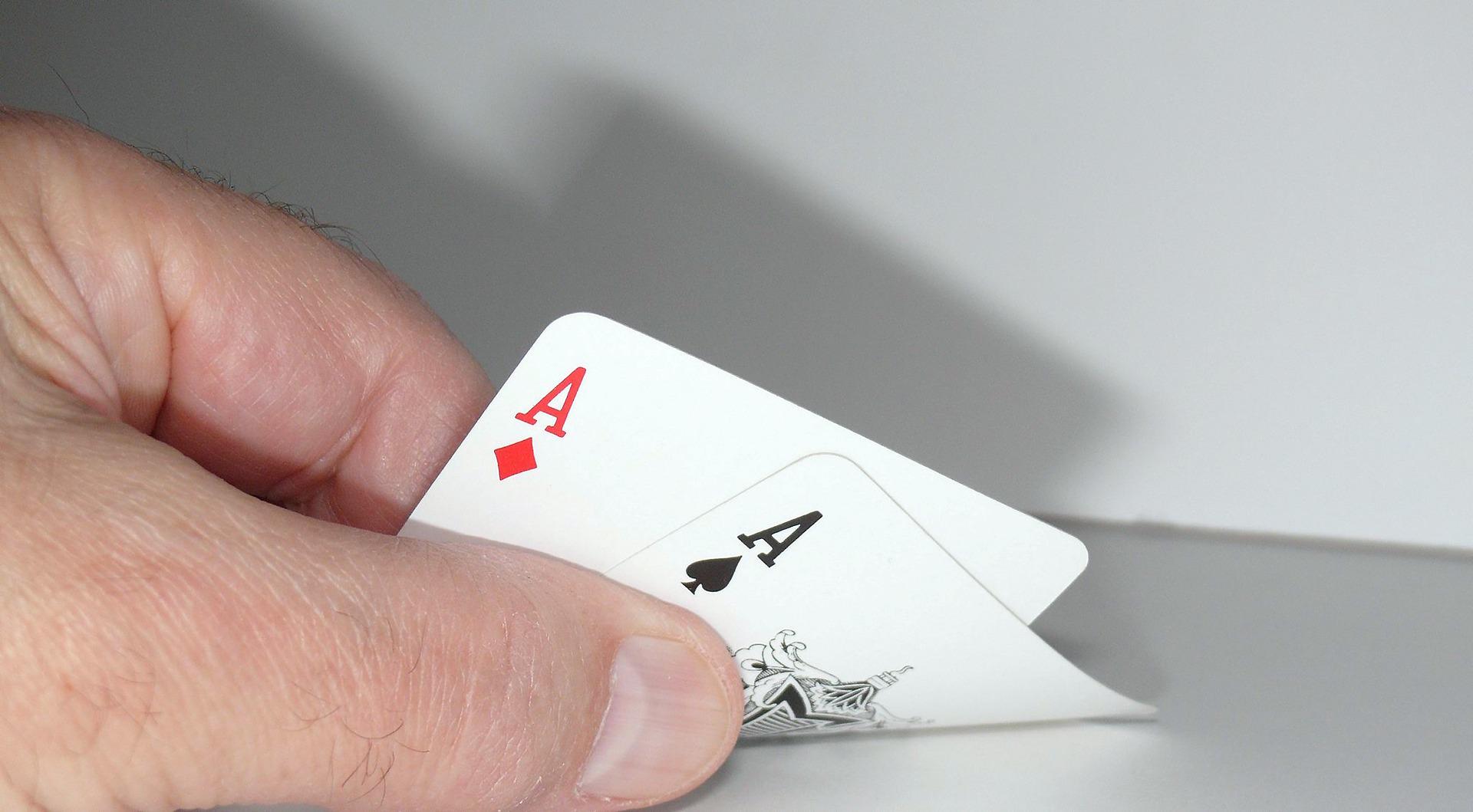 Poker Spielsituation: Ein Spieler betrachtet seine Handkarten und hält zwei Asse