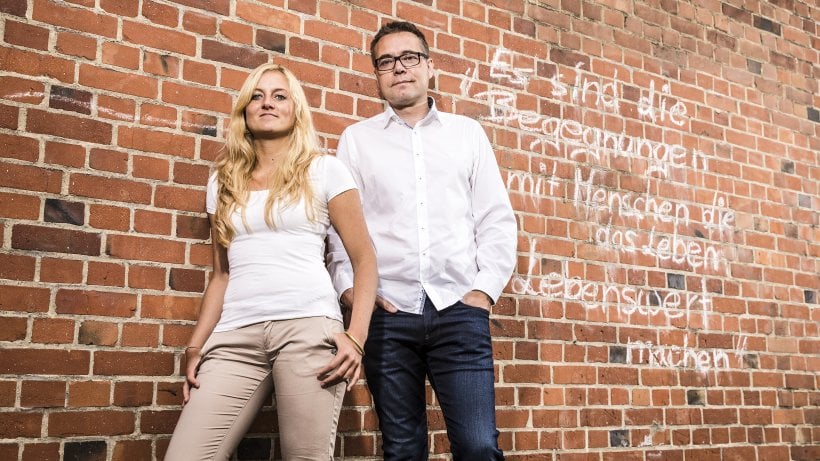 Steffen Moritz und seine Mitarbeiterin posieren vor einer Wand