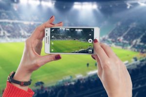 Frau hält Smartphone im Fußballstadion hoch