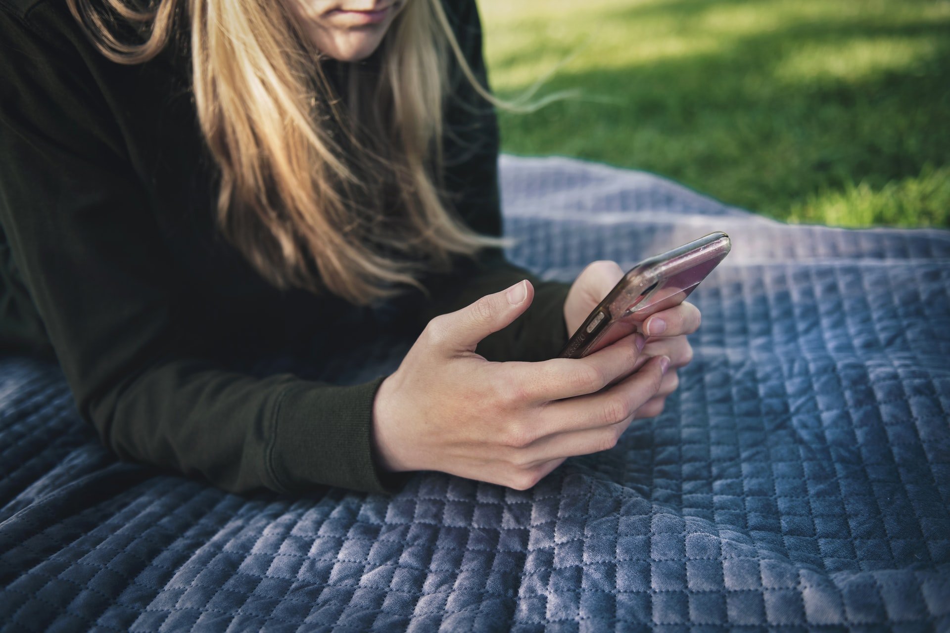 Frau liegt im Freien mit Handy in der Hand