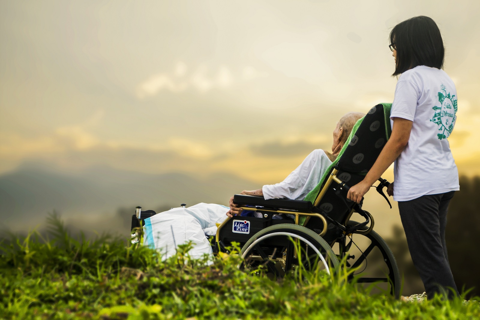 Altenpflege Pflegerin schiebt Patientin in Rollstuhl im Grünen