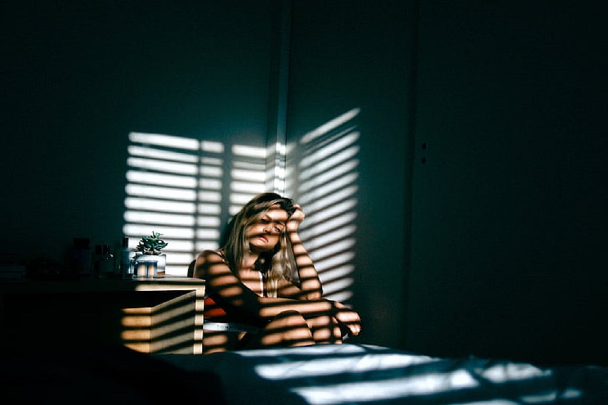 Frau sitzt in der Ecke eines Raums Fensterläden werfen Schatten