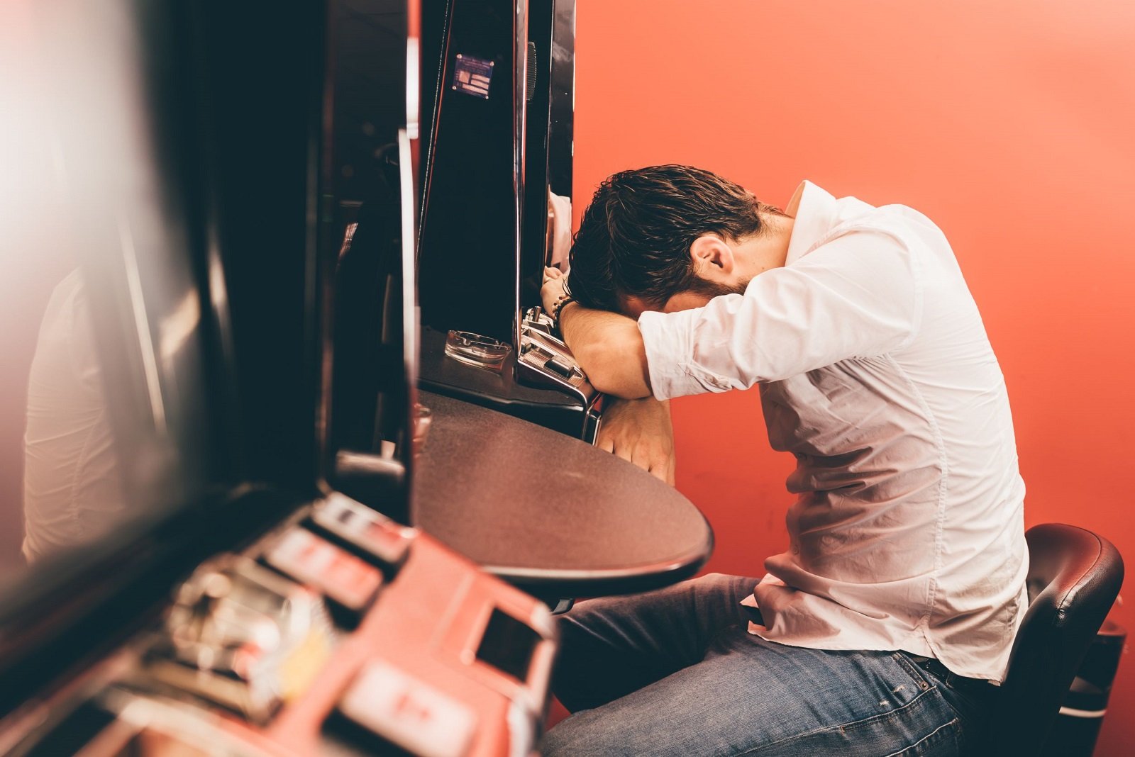 Mann am Spielautomaten stützt Kopf auf seine Arme