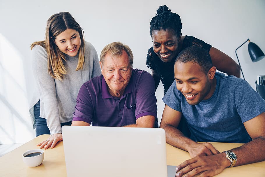 Vier Personen schauen auf einen Laptop und lachen