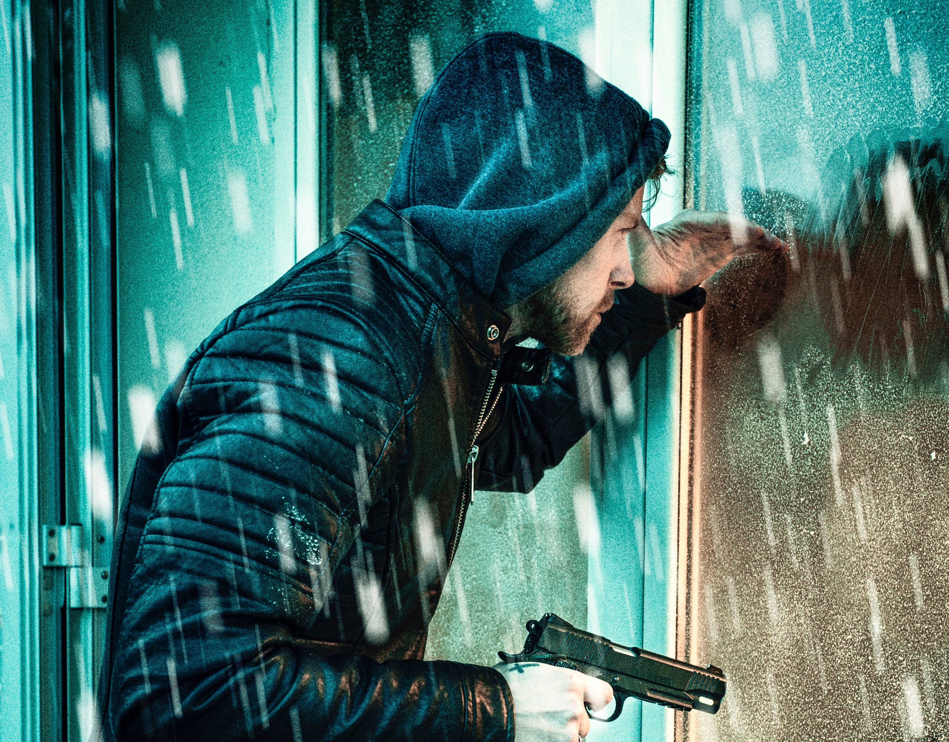 Mann mit Pistole schaut durch ein Fenster in ein Haus