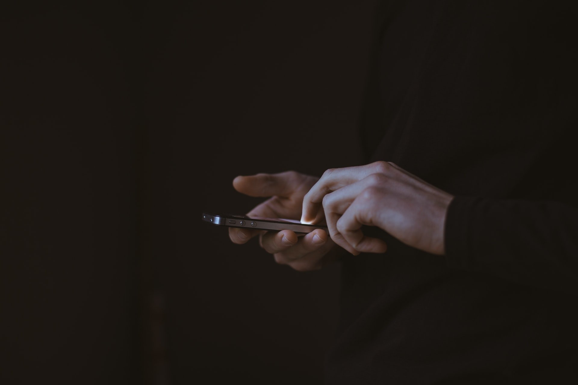 Mensch mit Handy in der Hand vor schwarzem Hintergrund