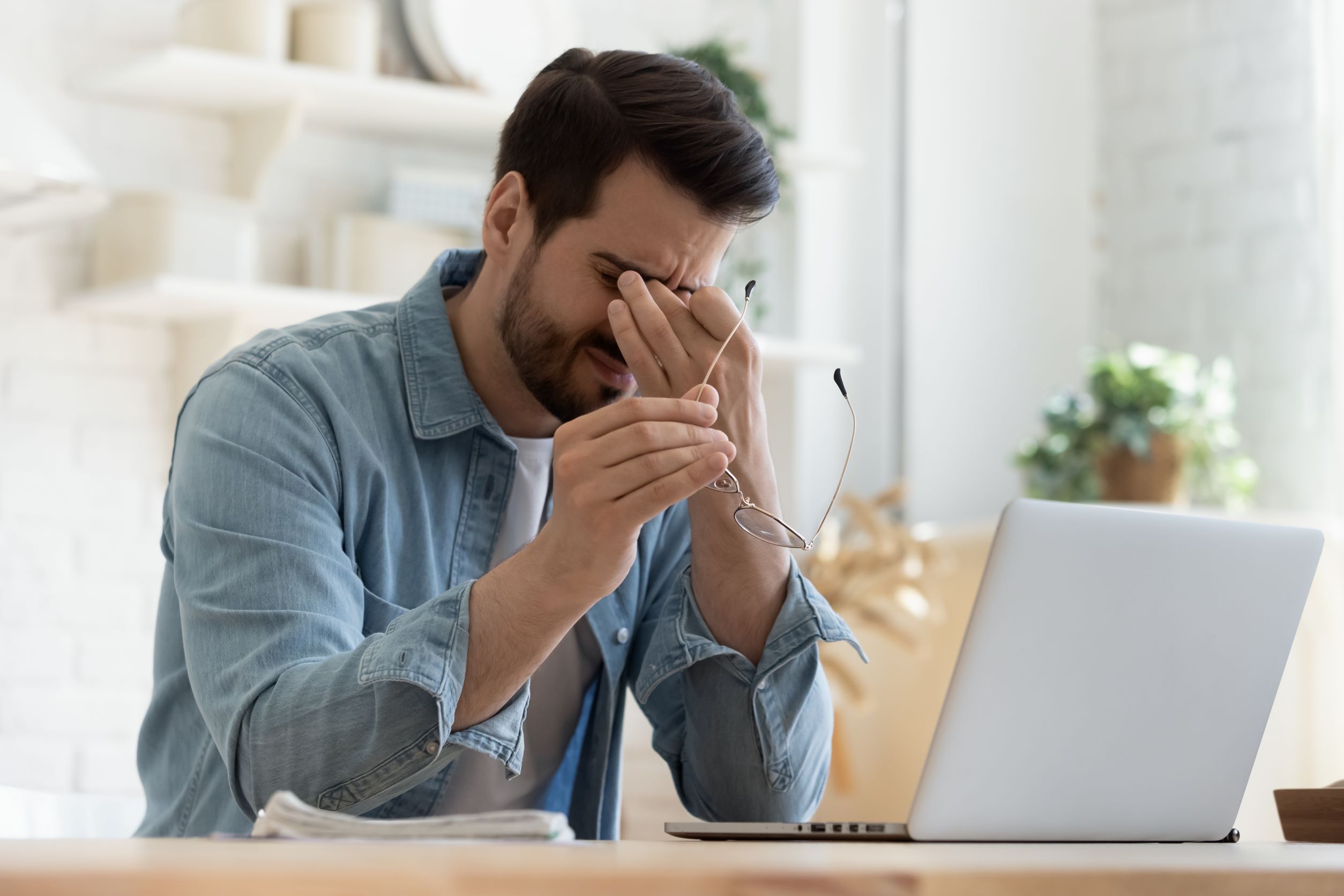 Mann vorm Laptop mit Brille in der Hand und einer Hand über den Augen